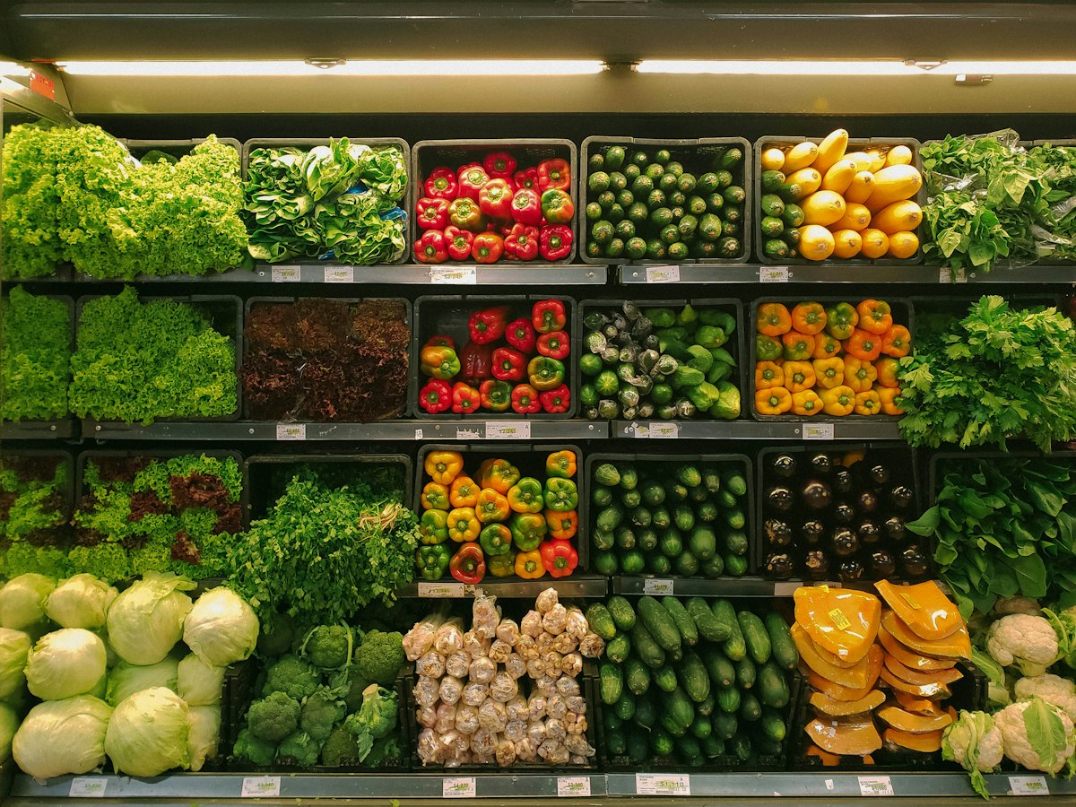A supermarket chiller display stacked with lettuces, peppers, courgettes, aubergines and other fresh vegetables.