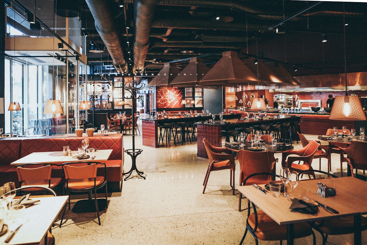 A large restaurant dining room with booths, an open kitchen counter and copper extractor hoods.