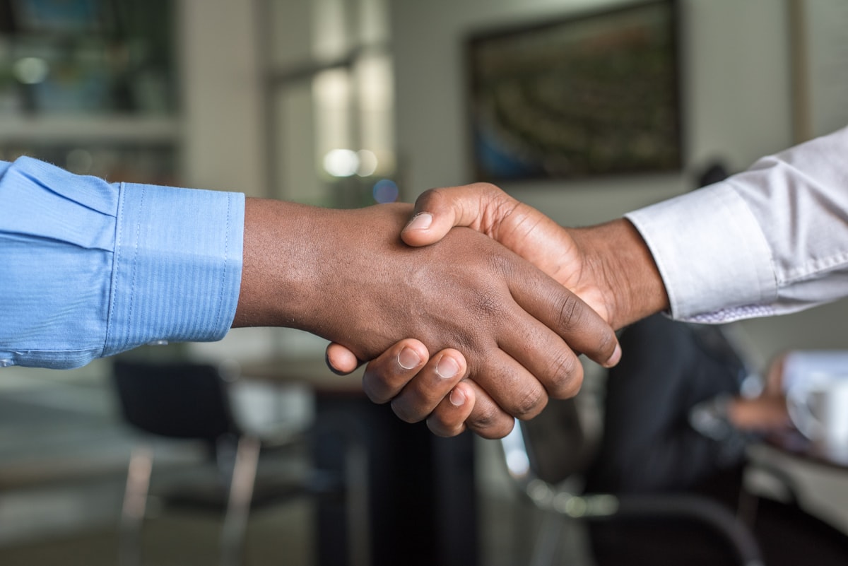 Two people in shirtsleeves shake hands across a meeting table in a bright office.