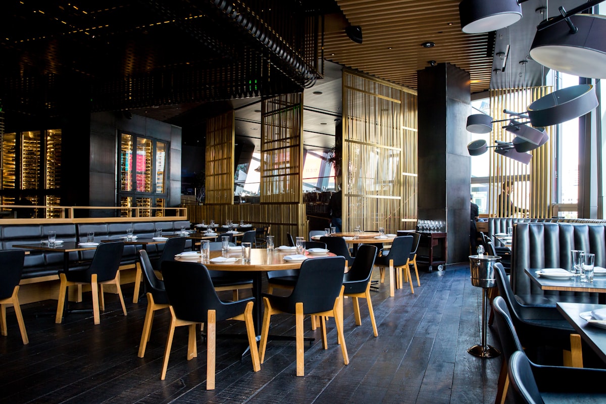 An empty modern restaurant dining room with laid tables, banquette seating and a glass wine store.
